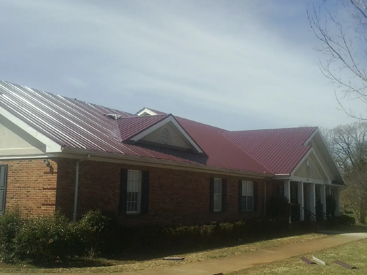 Red metal roof with gabled entries on a long brick building, from a Hail Damage Roof Repair job in Cuttyhunk