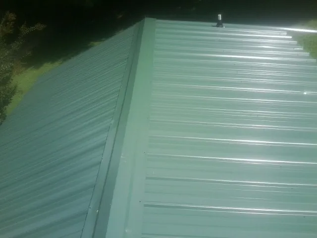 New green metal panels meeting at the ridge of a roof — Flat Roof Repair work by our crew in Cuttyhunk