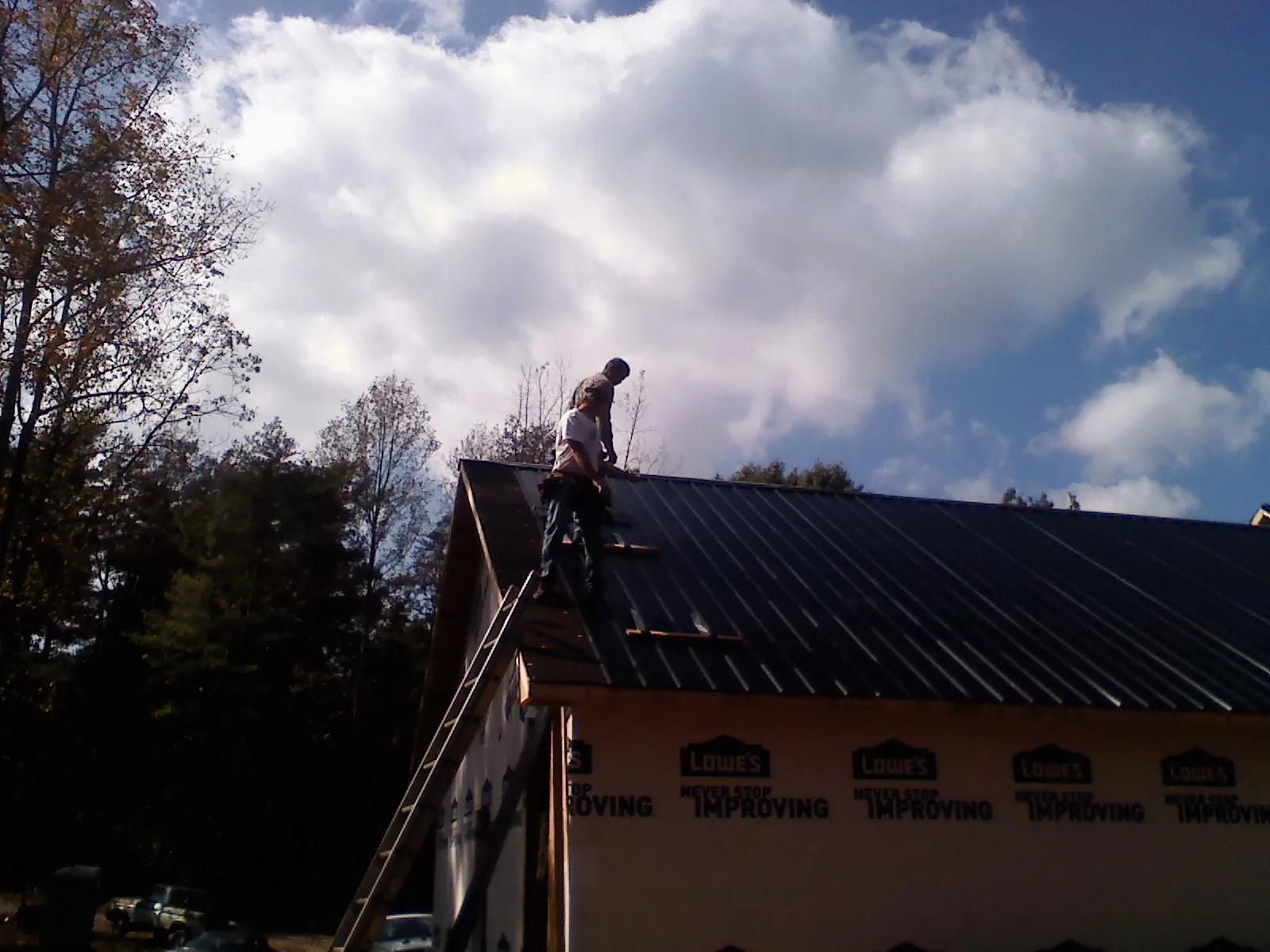 Roofer fastening dark metal panels high against a cloudy sky, from a Roof Inspection job in Cuttyhunk