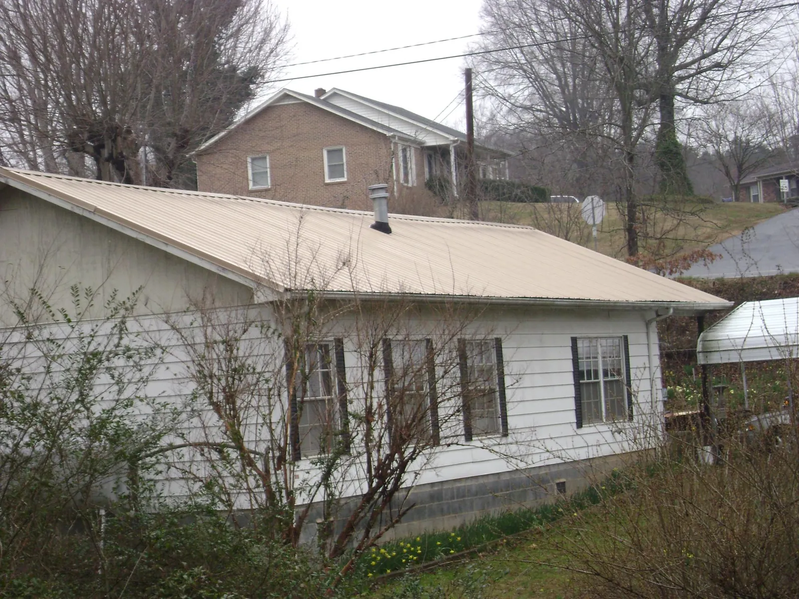 Tan metal roof on a white sided house set into a hillside — Commercial Roofing by Roofing Brothers in Cuttyhunk